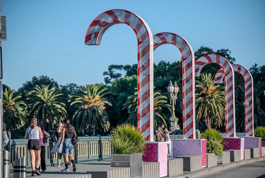 People walk by giant candy cane decorations with palm trees in background.