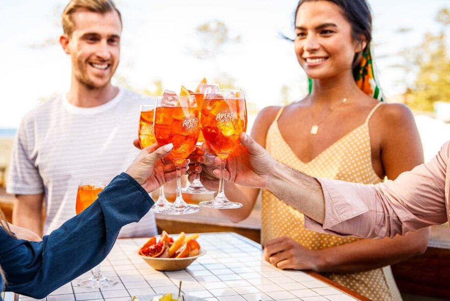 People clinking spritz Aperol cocktails at an outdoor bar table.