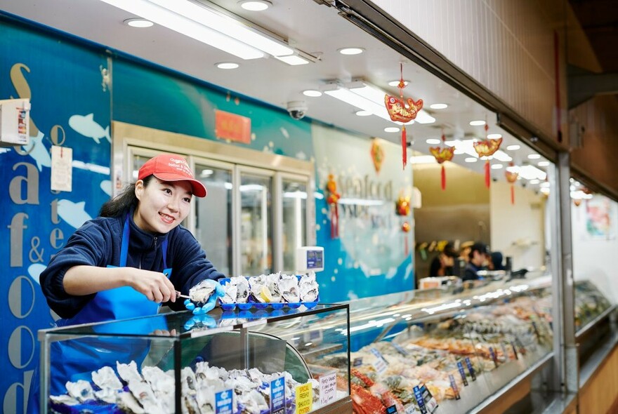 Smiling vendor offering seafood at Queen Victoria Market.