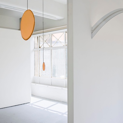 The white walls and light-filled gallery rooms at CAVES, with a large disc shaped sculpture hanging from the ceiling.