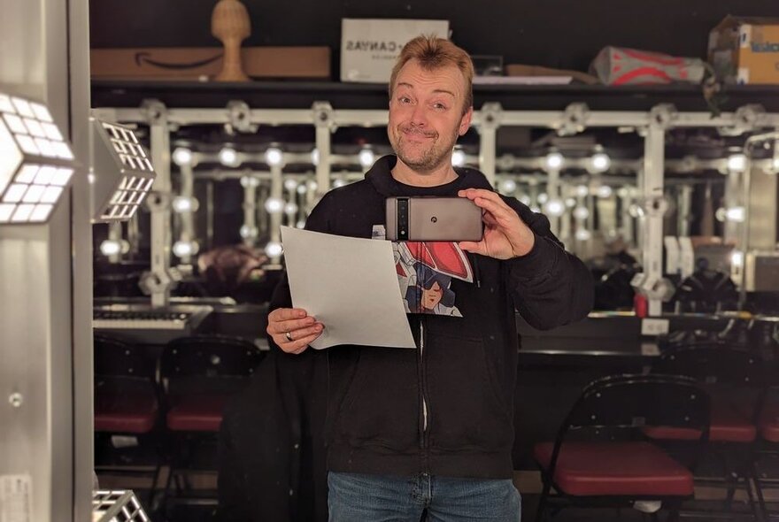 Man holding a piece of paper and an iPhone, standing in front of mirrors and barstools.