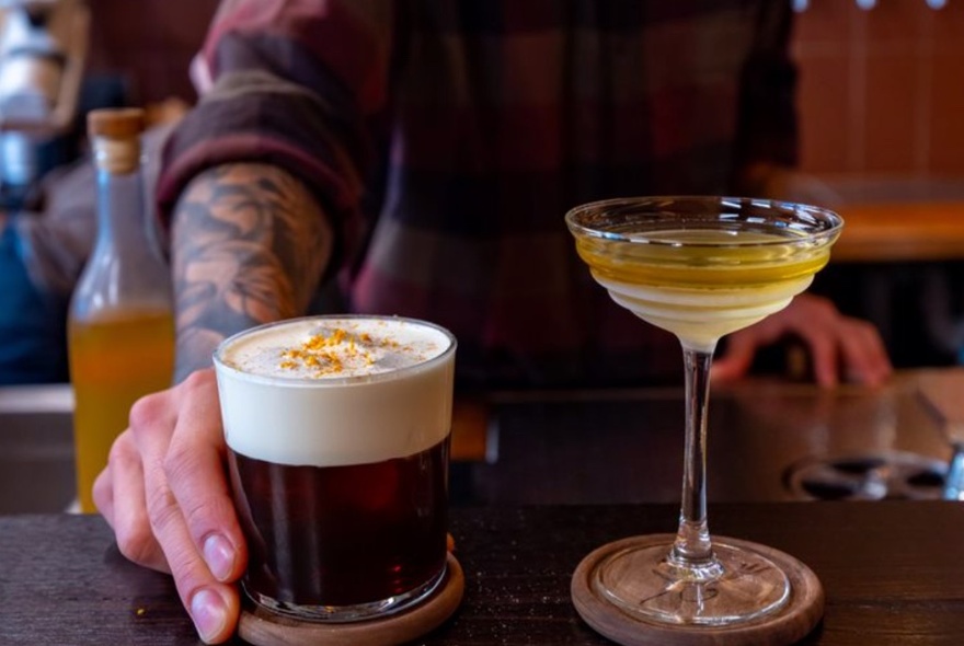 Hand holding coffee cocktail on bar, martini glass beside it.