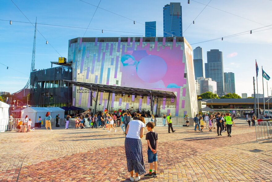A mother and son are at a festival at Federation Square on a sunny day