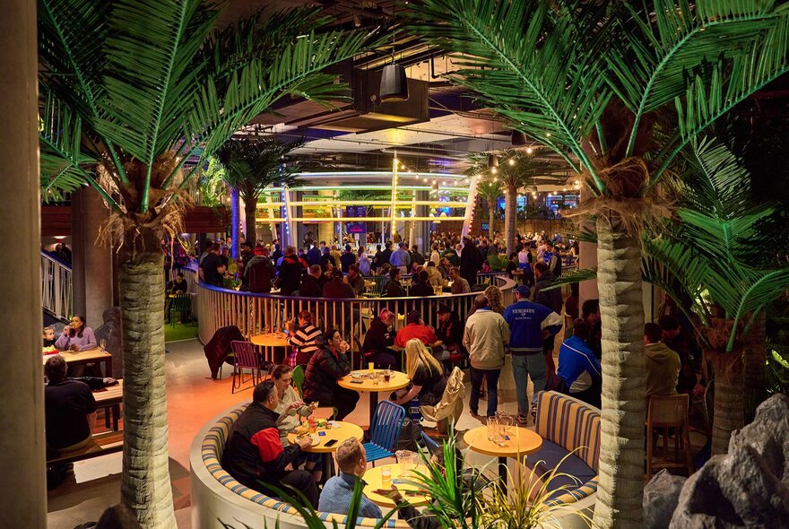 A busy beer garden with palm trees.