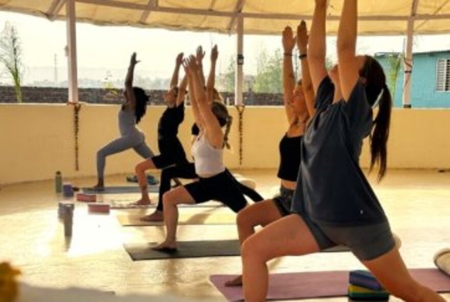 People indoors performing yoga moves with their hands in the air. 