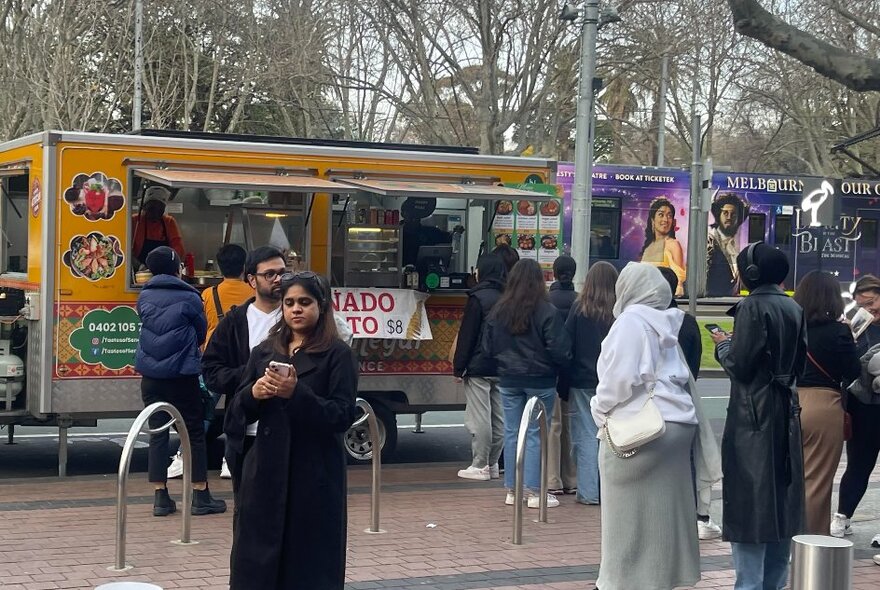 People queuing for takeaway food from a food truck with winter trees in the background.