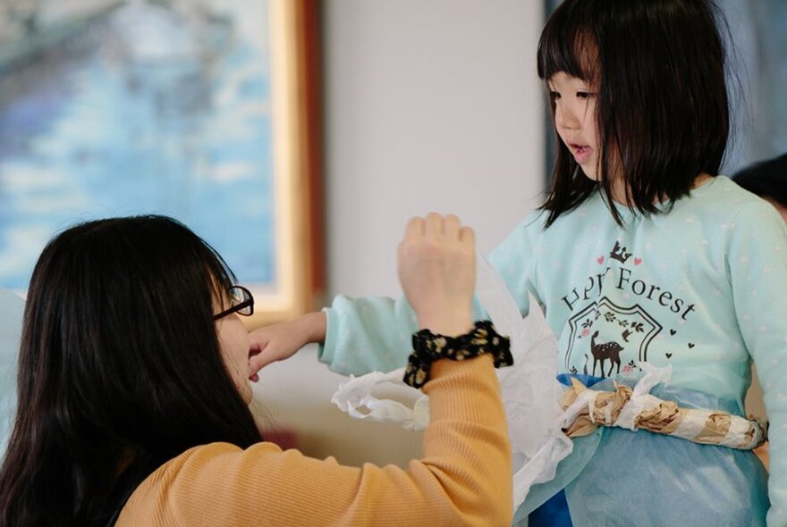 A woman kneeling down before a young girl, holding her hand up. 