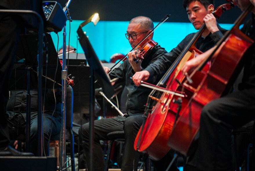 Two string musicians seated while performing on stage.