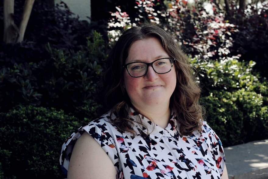 Woman with pierced lips and glasses with brown hair, in a garden.