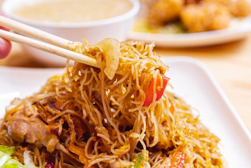 Chopsticks in a plate of stir fired noodles on a white plate.