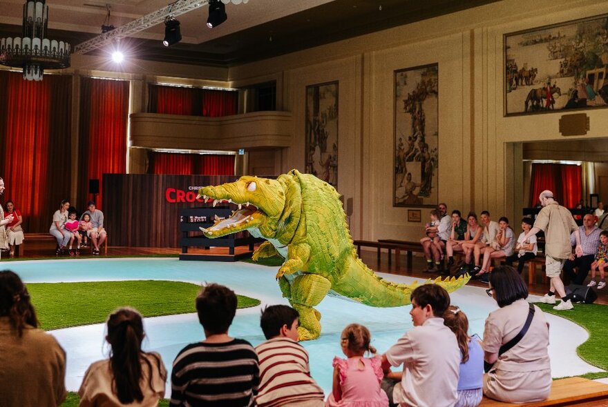 The large puppet croc show taking place in an open space at Myer Mural Hall, with seated children and families watching.