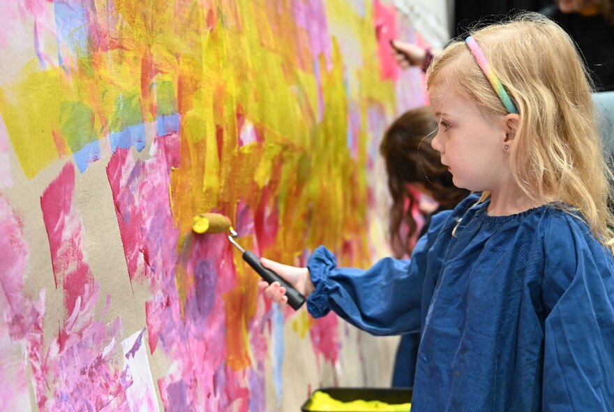 A young girl in an art smock, paining using a small roller. 