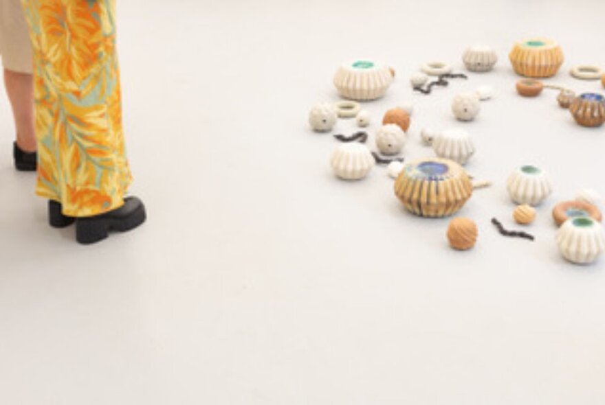 Legs and shoes of two people looking at an exhibit on the floor of round baskets of varying sizes.