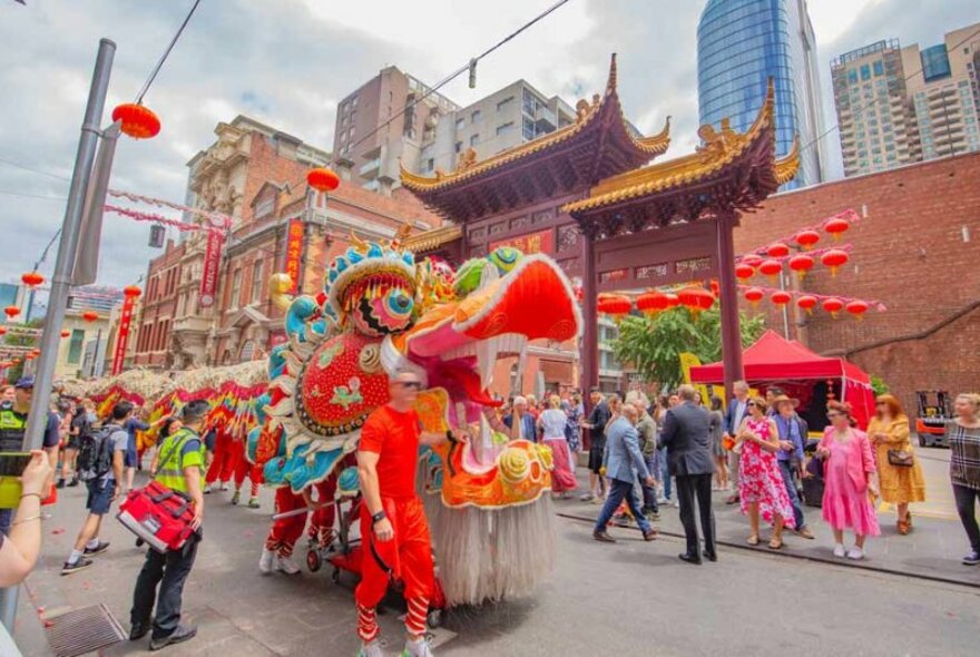 A parade of performers walking a long lion puppet down a street during Chinese Lunar New Year