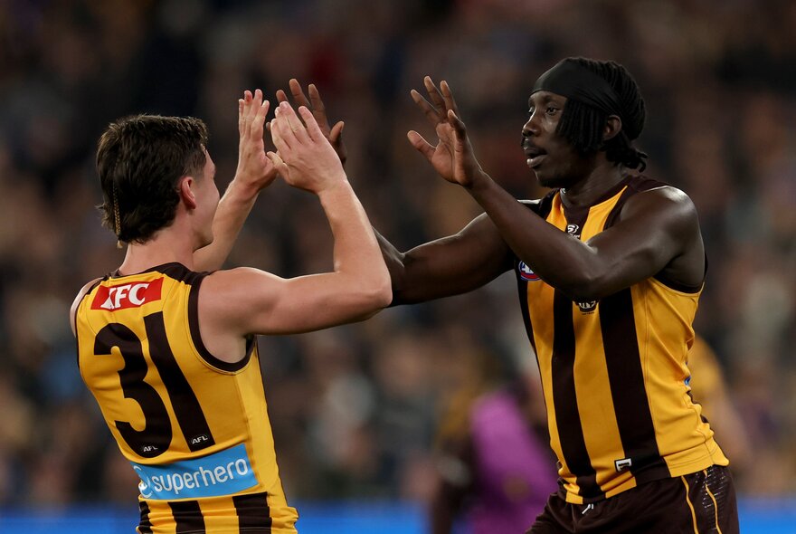 Two Hawthorn AFL players celebrating on the field with high-fives.
