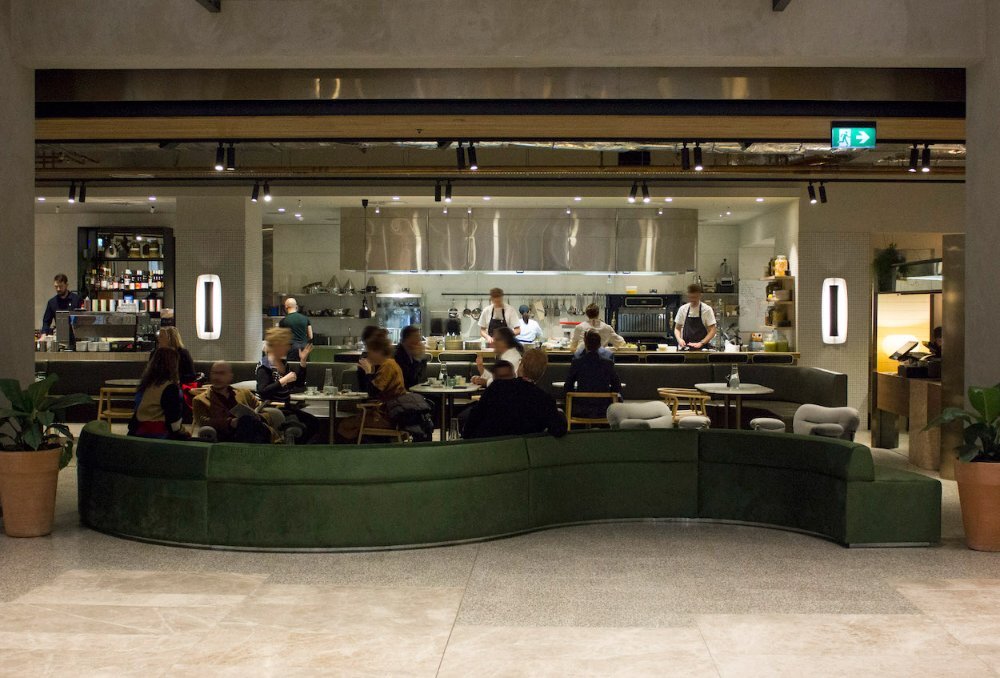 Dining room of busy cafe with a long green curved couch.