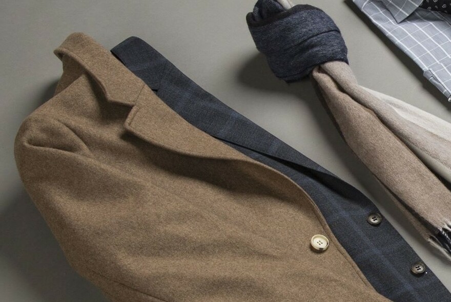 Brown and grey suit jackets on a table with folded scarbes.