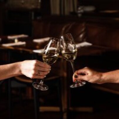 Two hands, each tapping a wine glass together in a toast.