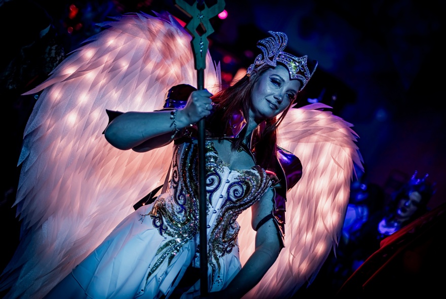 A woman in a warrior queen costume with a large staff and fairy wings behind her. 