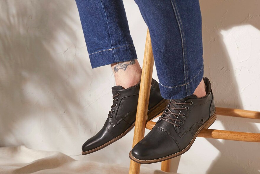 Detail of woman's feet wearing jeans and brown leather lace-up shoes.