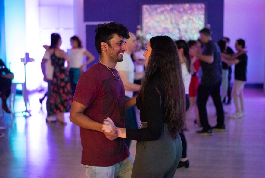 A couple dancing with hands clasped on a dance floor with purple lights.