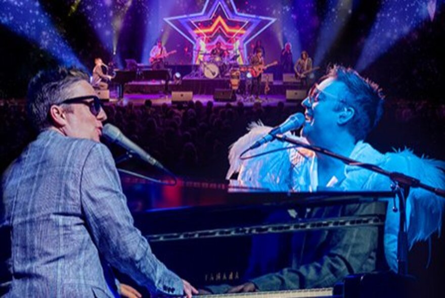 A man playing piano dressed up like Elton John and also Billy Joel, with a band in the background.