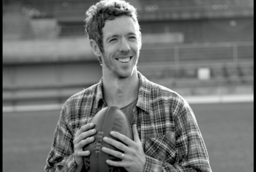 Black and white image of ex-footballer and ABC broadcaster Bob Murphy, holding a football and smiling openly.
