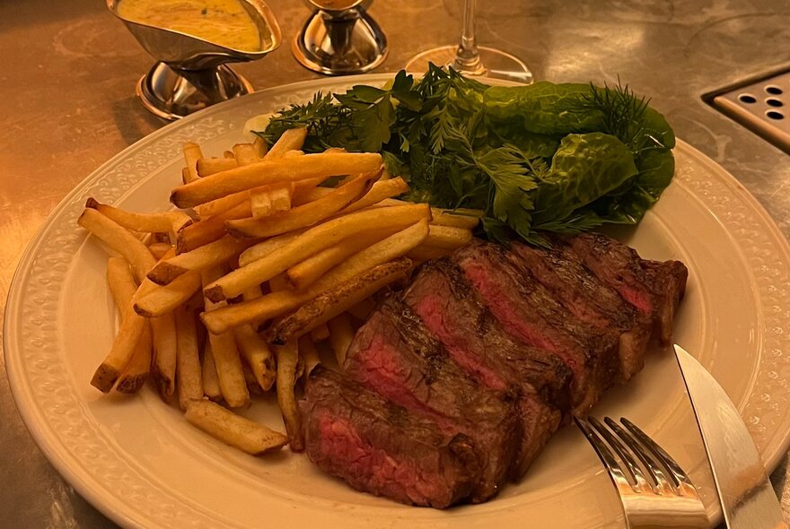 A rare steak with chips, salad and a gravy boat.