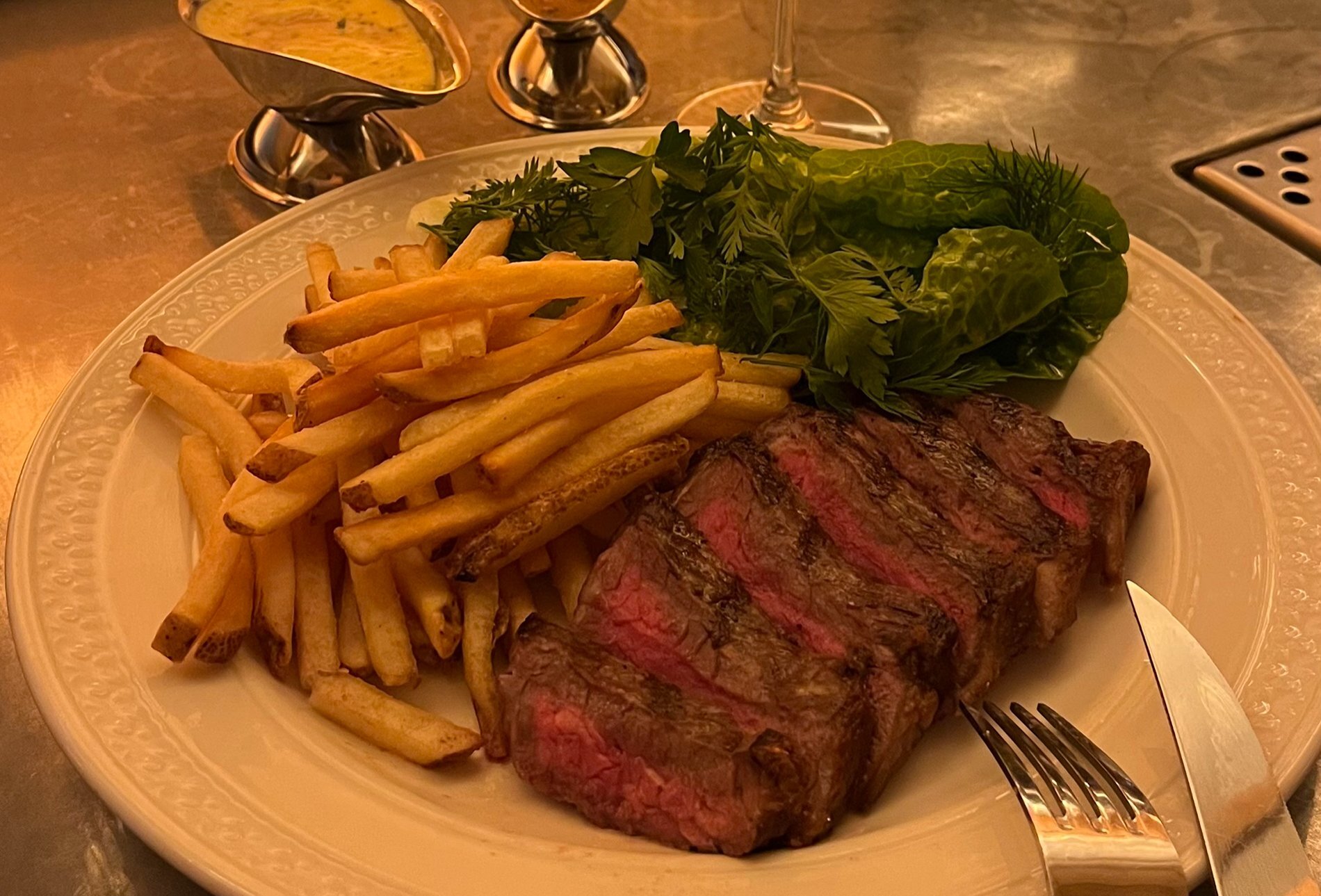 A rare steak with chips, salad and a gravy boat.
