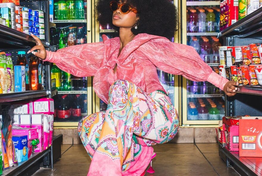 A fashion model modelling an outfit while crouched down in the aisle of a supermarket.