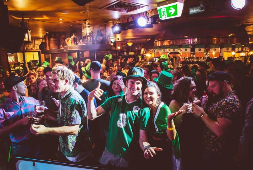 A lively St. Patrick's Day celebration at a crowded Irish pub in Melbourne, featuring patrons dressed in festive green attire. 
