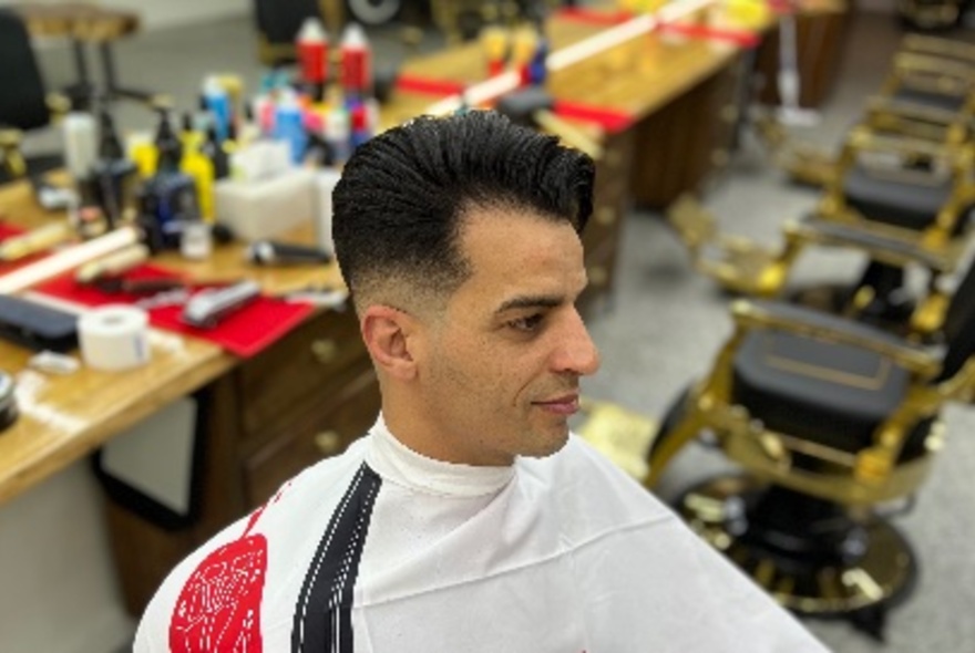 A man seated in a chair in a barber's shop, with freshly cut and styled hair.