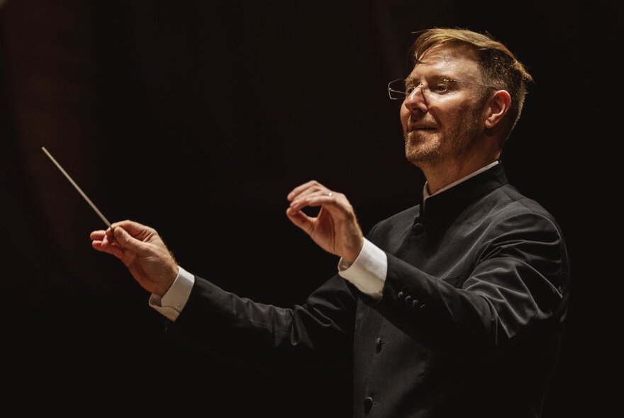 Finnish composer Jean Sibelius conducting with hands and baton up. 