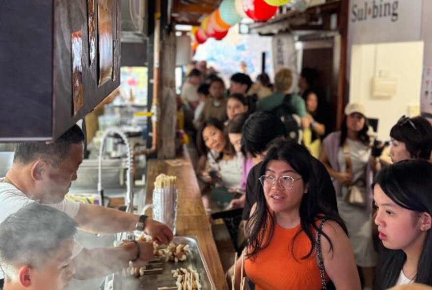 People lining up to order at a food stall in a outdoor type hall. 