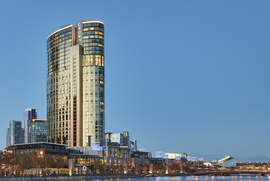 Crown Towers at dusk with illuminated mirror windows in the tower and ground-level facilities stretching along the Yarra River.