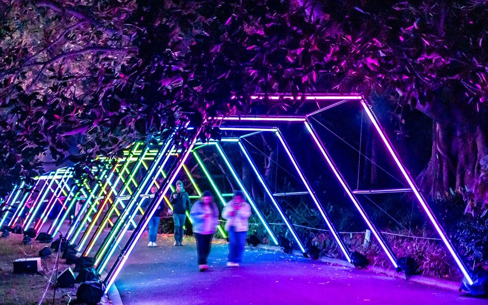 People walking through a tunnel of angular neon lights.