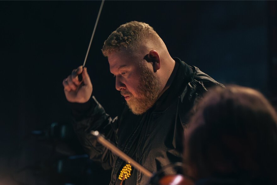 Australian Art Orchestra Artistic Director, Aaron Choulai, conducting while wearing a leather jacket and gold pendant.