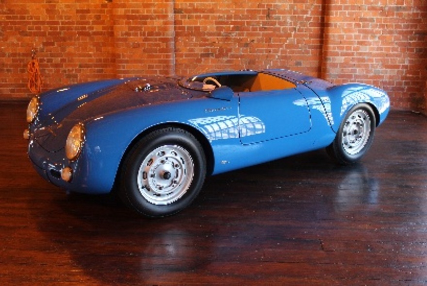 A blue sports car on display in a showroom, set against a red brick wall.