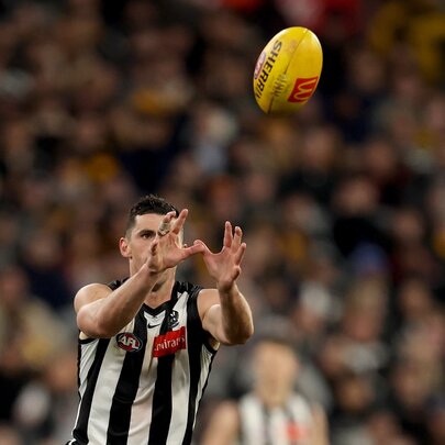 A Collingwood AFL player with his hands raised above him about to take a mark on the footy field, a blurred crowd of fans behind him.