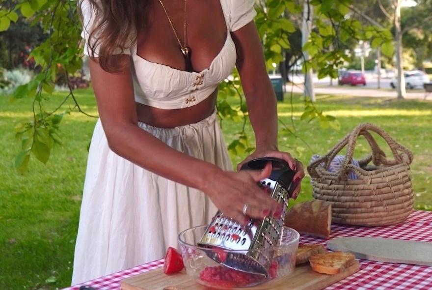 A woman in a white dress grating vegetables into a glass bowl, as part of a cooking class.