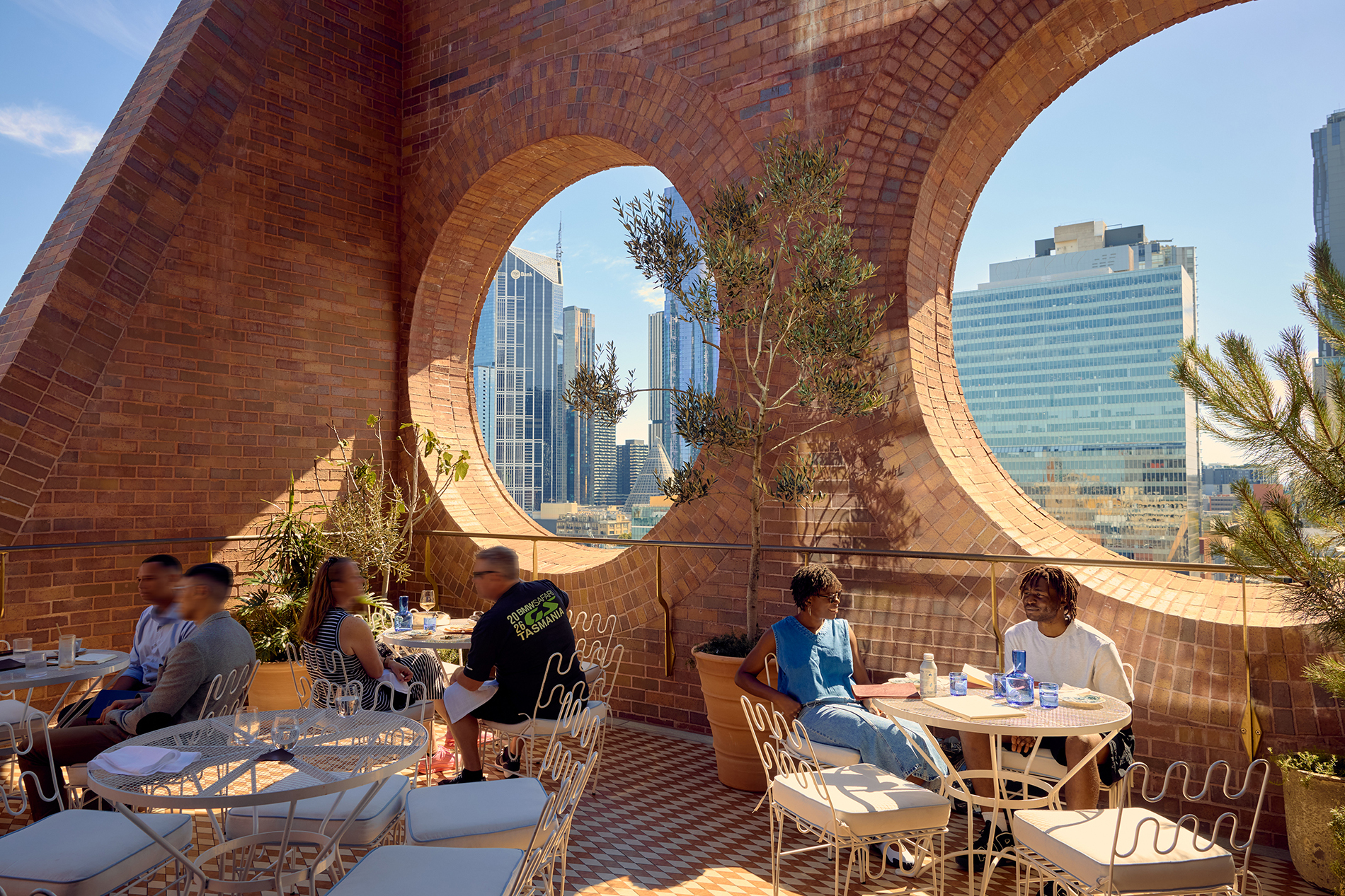 People sitting on a sunny rooftop next to circular cut outs in the brick wall.
