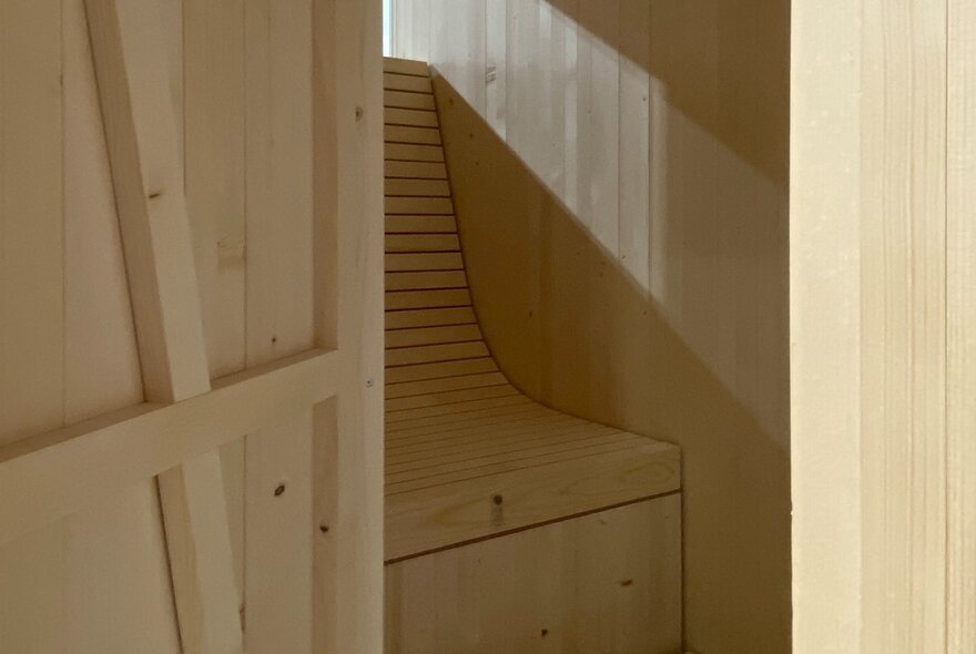 A pine sauna with the door open to reveal a single seat. 