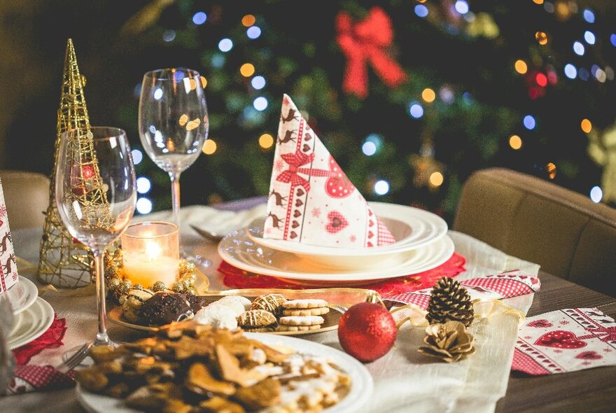 Festive table setting with decorated napkin, wine glasses, baubles and plates of biscuits.