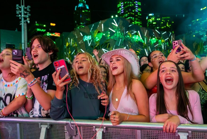 Audience members enjoying themselves at a concert, singing and holding up smartphones.