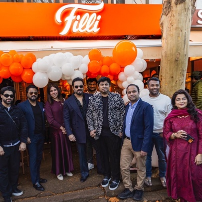 The well-dressed Filli cafe owners and their family standing outside the Filli cafe on its grand opening day, orange and white balloons behind them.