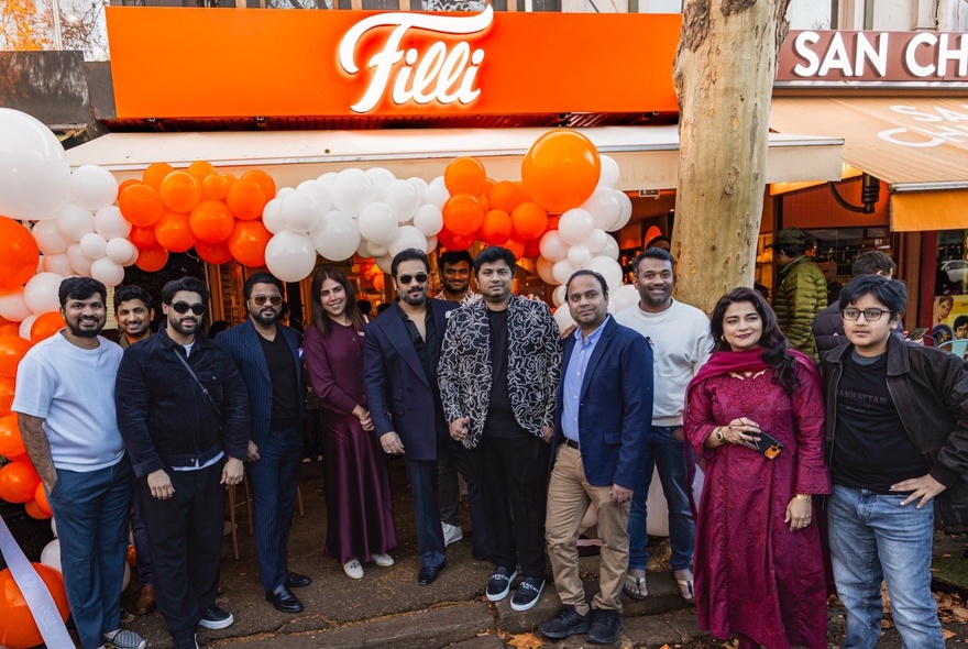 The well-dressed Filli cafe owners and their family standing outside the Filli cafe on its grand opening day, orange and white balloons behind them.