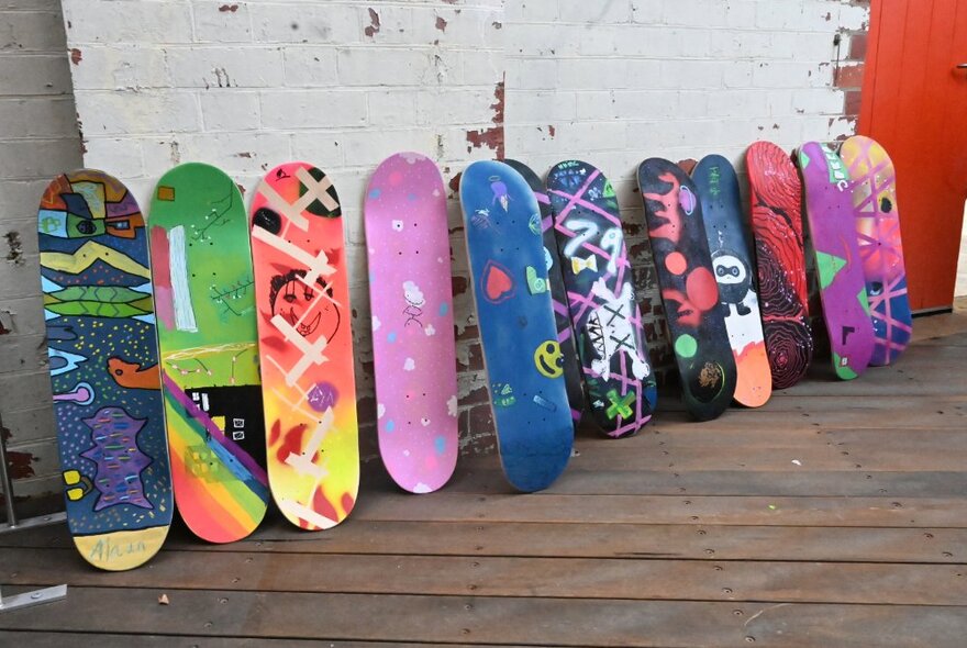 Bright, hand painted skateboards all lined up against a wall.