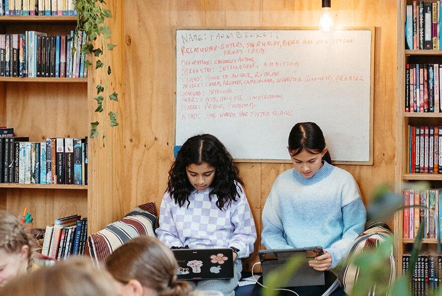 Two children seated on a sofa working on laptops.