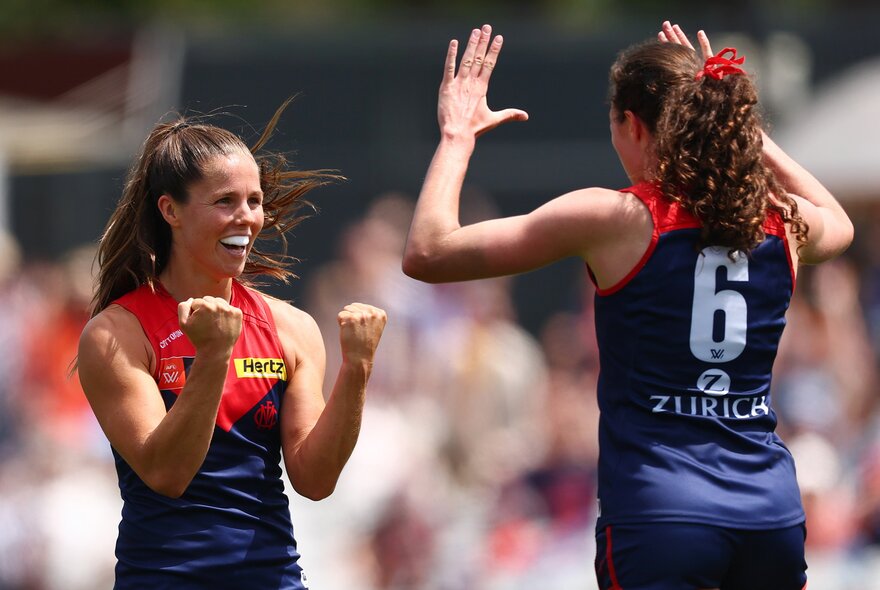 Melbourne AFLW players making fists and high-fiving during a match.
