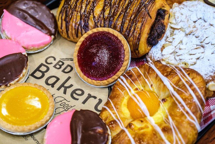 A selection of sweet pastries, jam tarts, and chocolate eclairs on display.